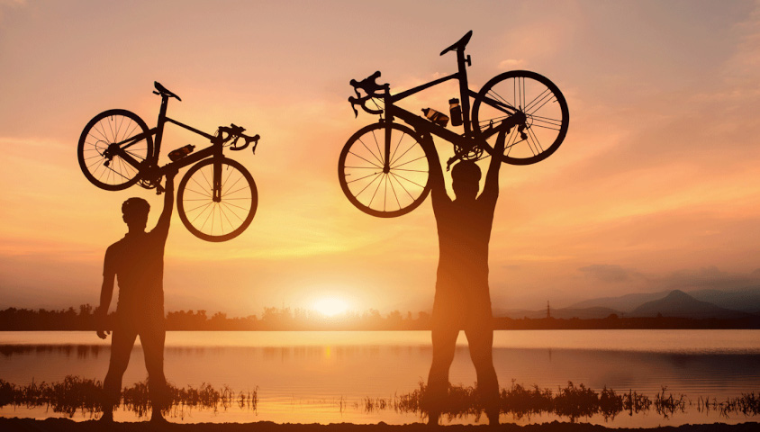 Radfahrer mit Fahrrädern über dem Kopf im Sonnenuntergang